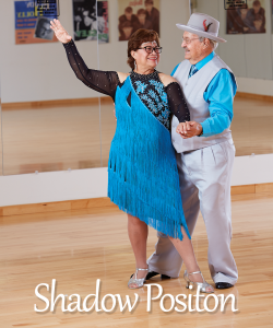 Showmanship and Promotion - Love often urges us to put the spotlight on our partner; a common goal may require us to promote our partner’s skills. Togetherness takes a different shape when we must lead from behind, or face the public on behalf of our partner in the wings. The “Shadow Position” seen in many ballroom dances and in couples figure skating, represents this kind of relationship. The man dances behind the woman for several measures of music. The couple holds hands as a way of keeping balance and communicating. Senior Instructors David and Lea Twigg demonstrate the “Shadow Position” as David shows off Lea and they both express a deep enjoyment of the dance and each other.