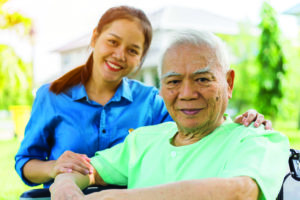 Portrait of Young caregiver in uniform hugging smiling elderly man or patient in wheelchair during a home visit and spending time together. Love, Family or Assistant or elderly caregiver concept
