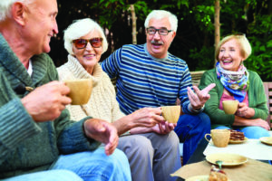 Cheerful group of senior friends enjoying each others company while having tea party at lovely patio, they wearing knitted sweaters