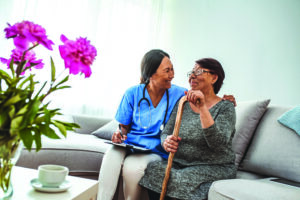 Friendly doctor examining health of patient at home. Happy smiling nurse consulting disabled patient about treatment. Nurse caring about elder handicap woman at home.