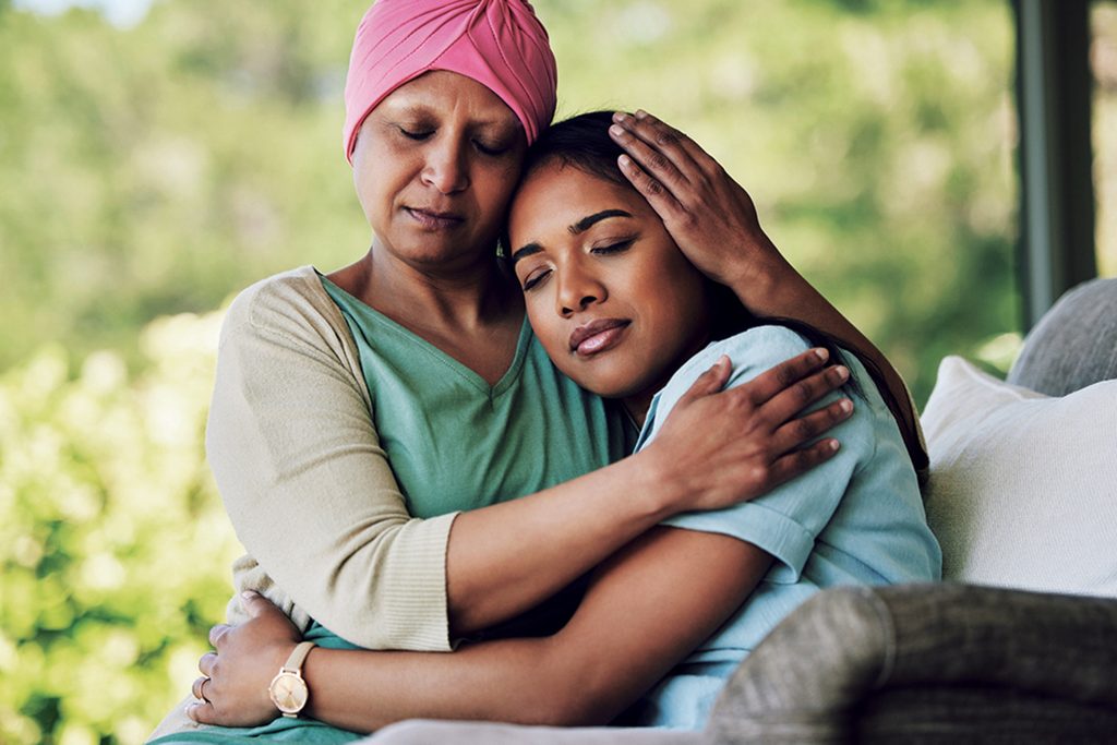Family, old woman hugging her daughter and cancer with sad people on a sofa in the home living room during recovery. Love, trust or comfort with a sick senior female parent embracing an adult child